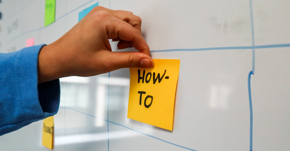 "how to" written on a sticky note, placed on a whiteboard
